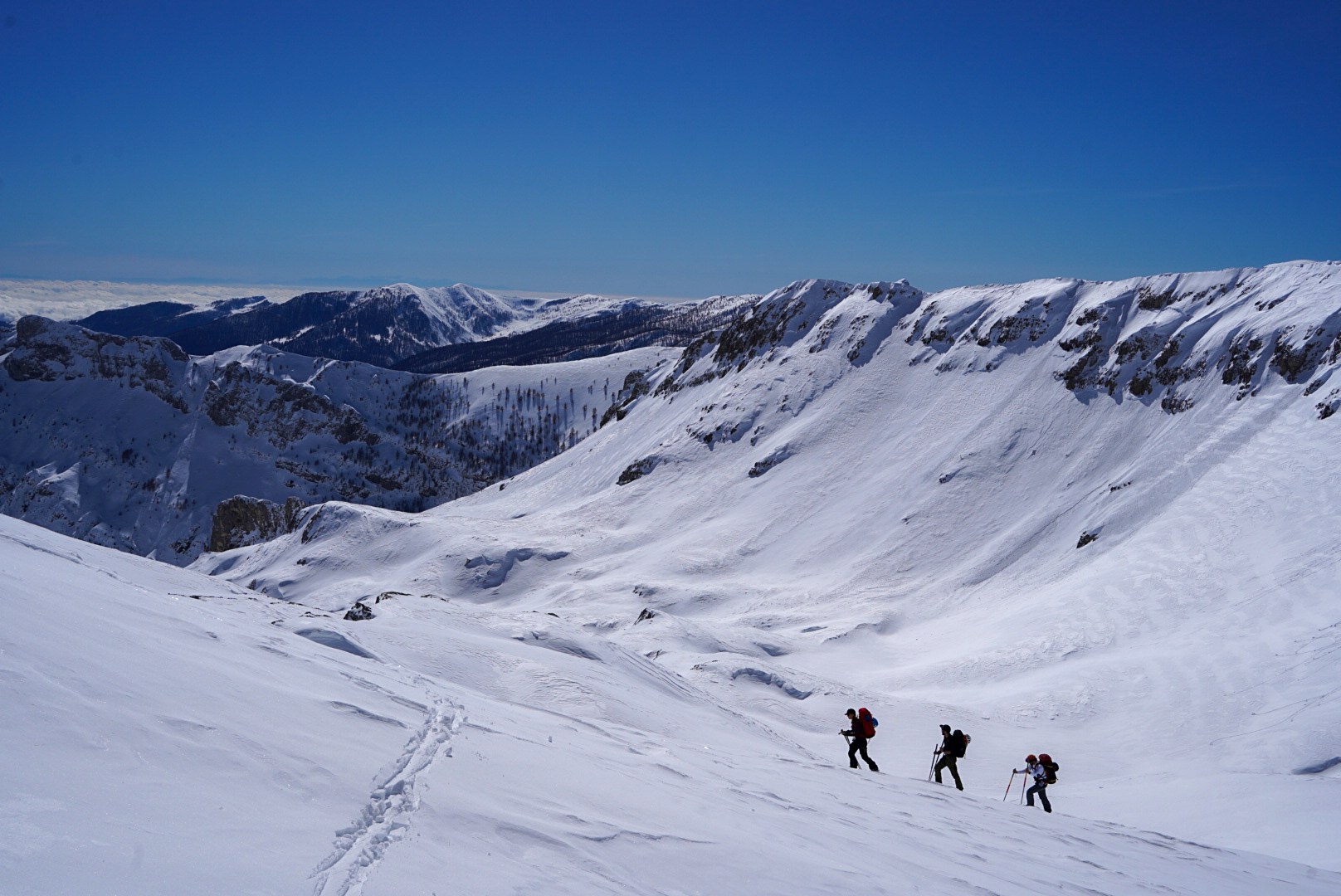 Trois skieurs progressant dans un vaste cirque enneigé, vallée de Becho, vers le massif de l’Ushba, pendant le voyage à ski en Géorgie.