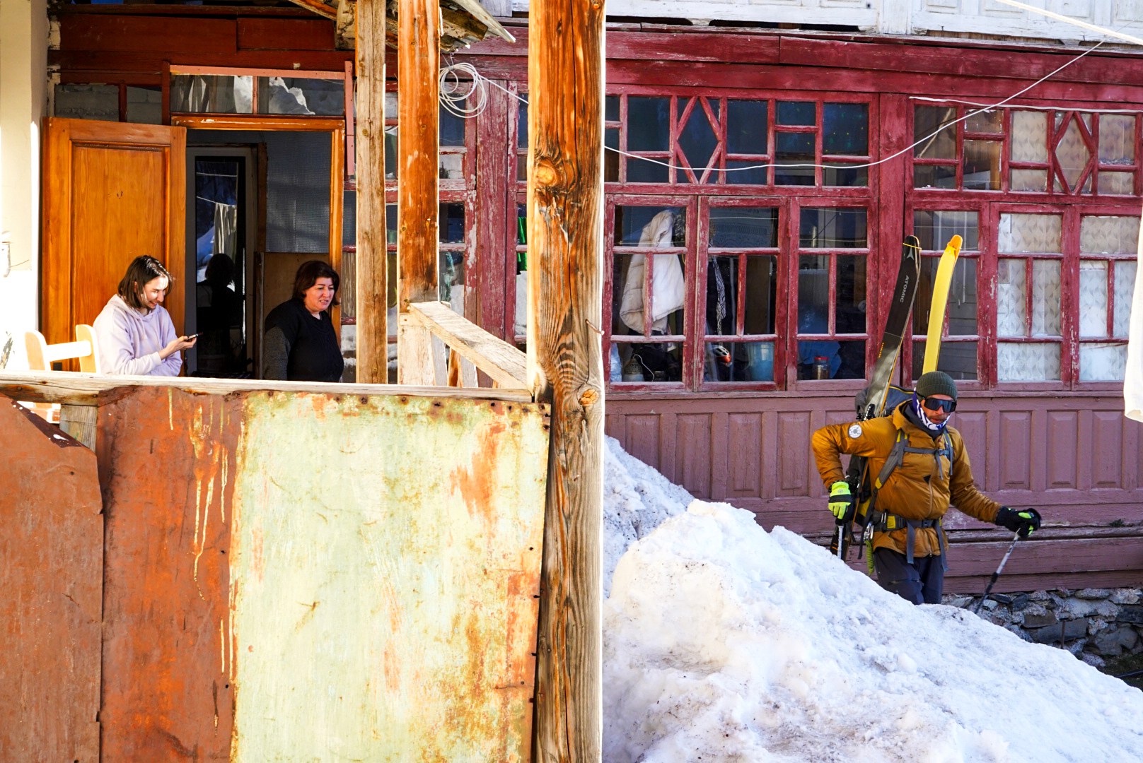Skieur portant ses skis devant une habitation, secteur d’Adishi et du Tetnuldi, pendant une traversée à ski en Haute-Svanétie.