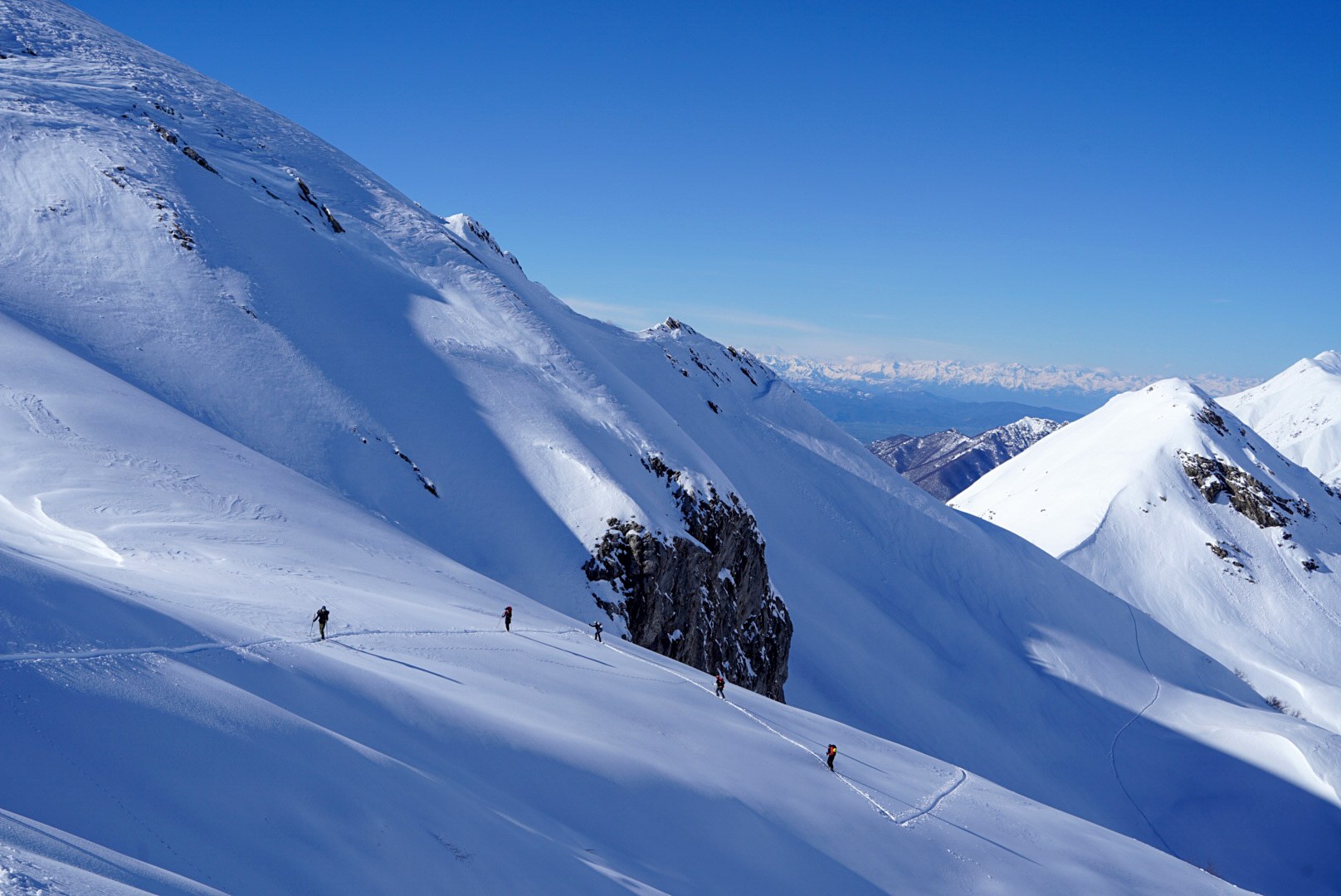 Skieurs avançant sur une pente avec les sommets de svanétie en arrière-plan, vallée de Becho, vers le massif de l’Ushba, pendant le voyage à ski en Géorgie.