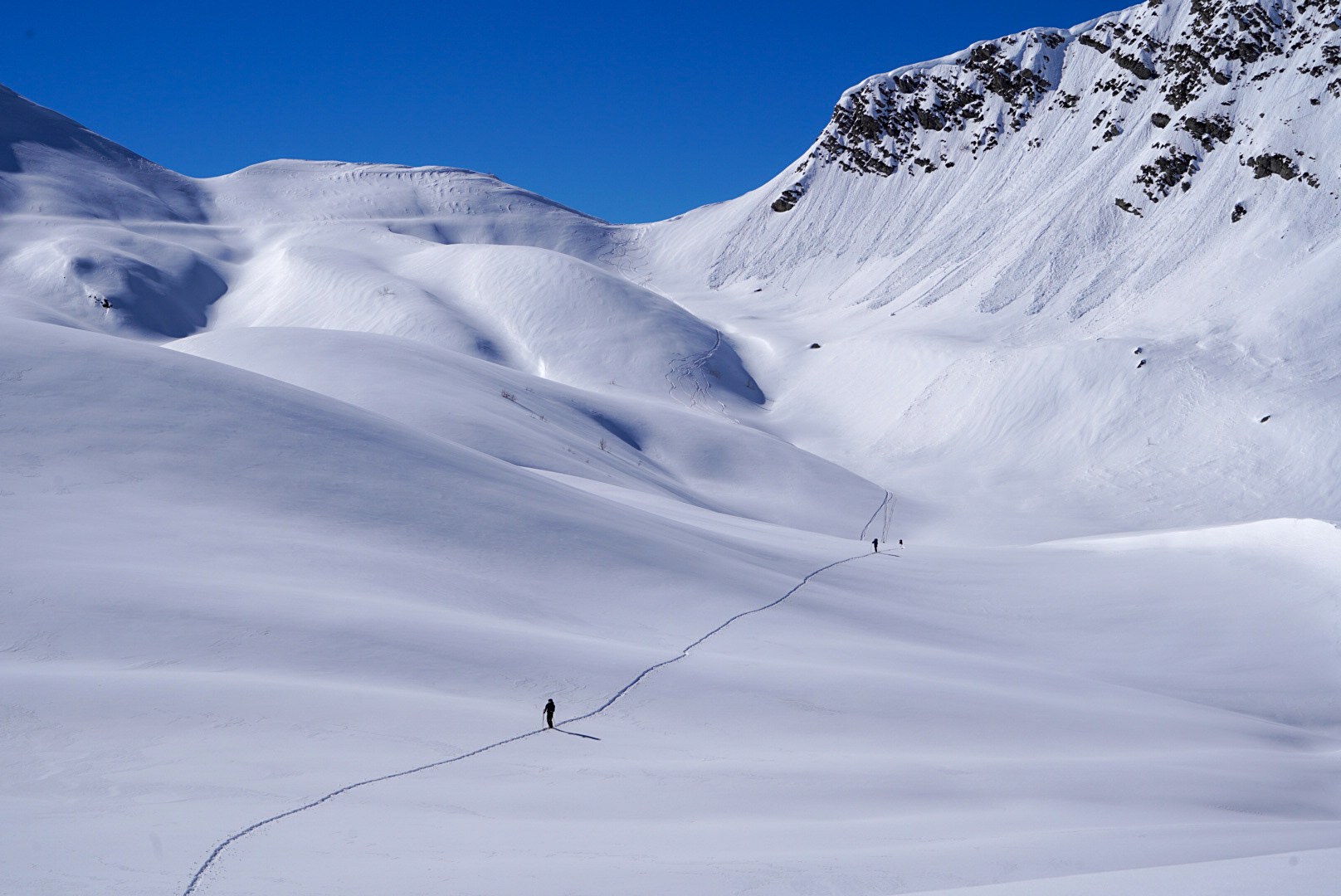 Deux skieurs traversant des ondulations de neige immaculée, vallée de Becho, vers le massif de l’Ushba, pendant le voyage à ski en Géorgie.