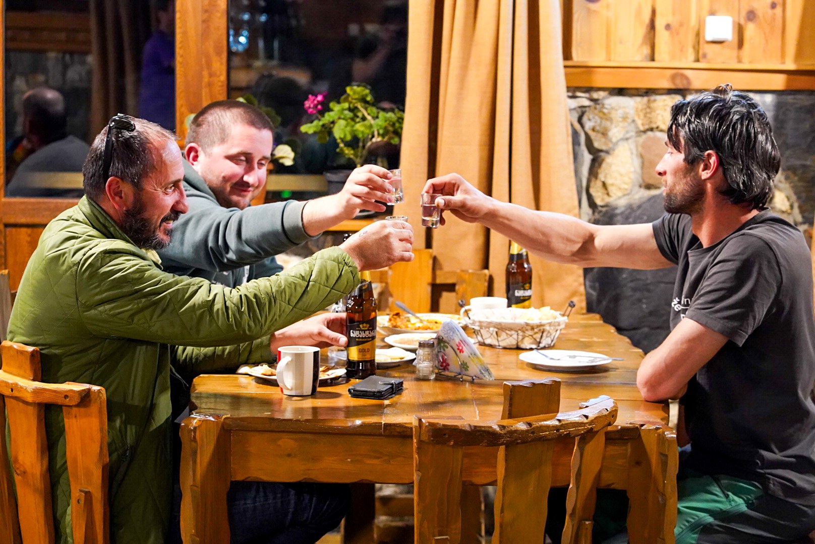 Compagnons levant leur verre autour d’une table en bois, route de Tbilissi à Mestia et arrivée en Svanétie, pendant le voyage à ski en Géorgie.