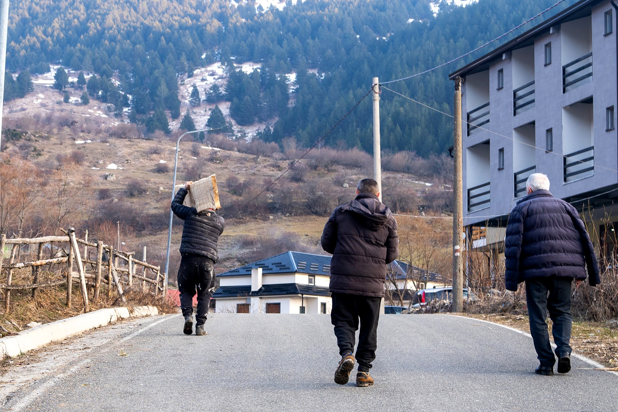 Compagnons traversant une rue bordée de maisons, secteur occidental du massif du Šar, près du Korab, pendant une traversée à ski du Kosovo.