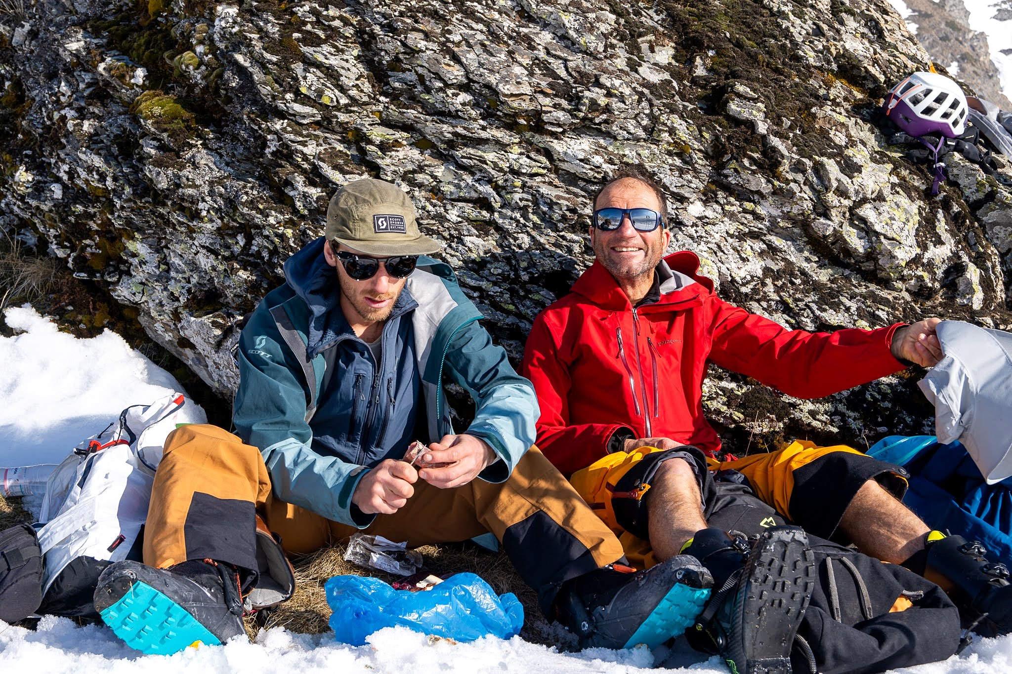 Deux compagnons déjeunant contre des rochers, secteur occidental du massif du Šar, près du Korab, pendant une traversée à ski du Kosovo.