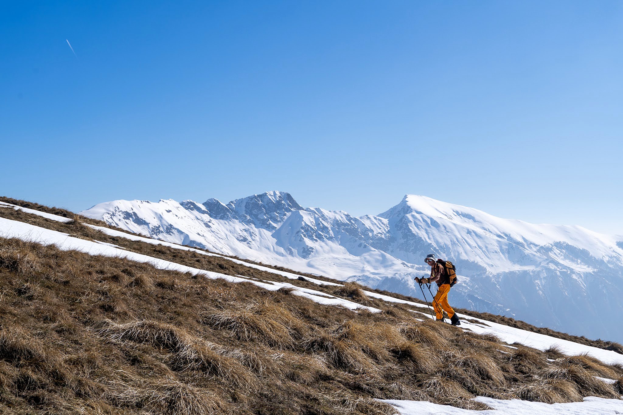 Skieur portant ses skis sur un versant encore herbeux, secteur occidental du massif du Šar, près du Korab, pendant une traversée à ski du Kosovo.