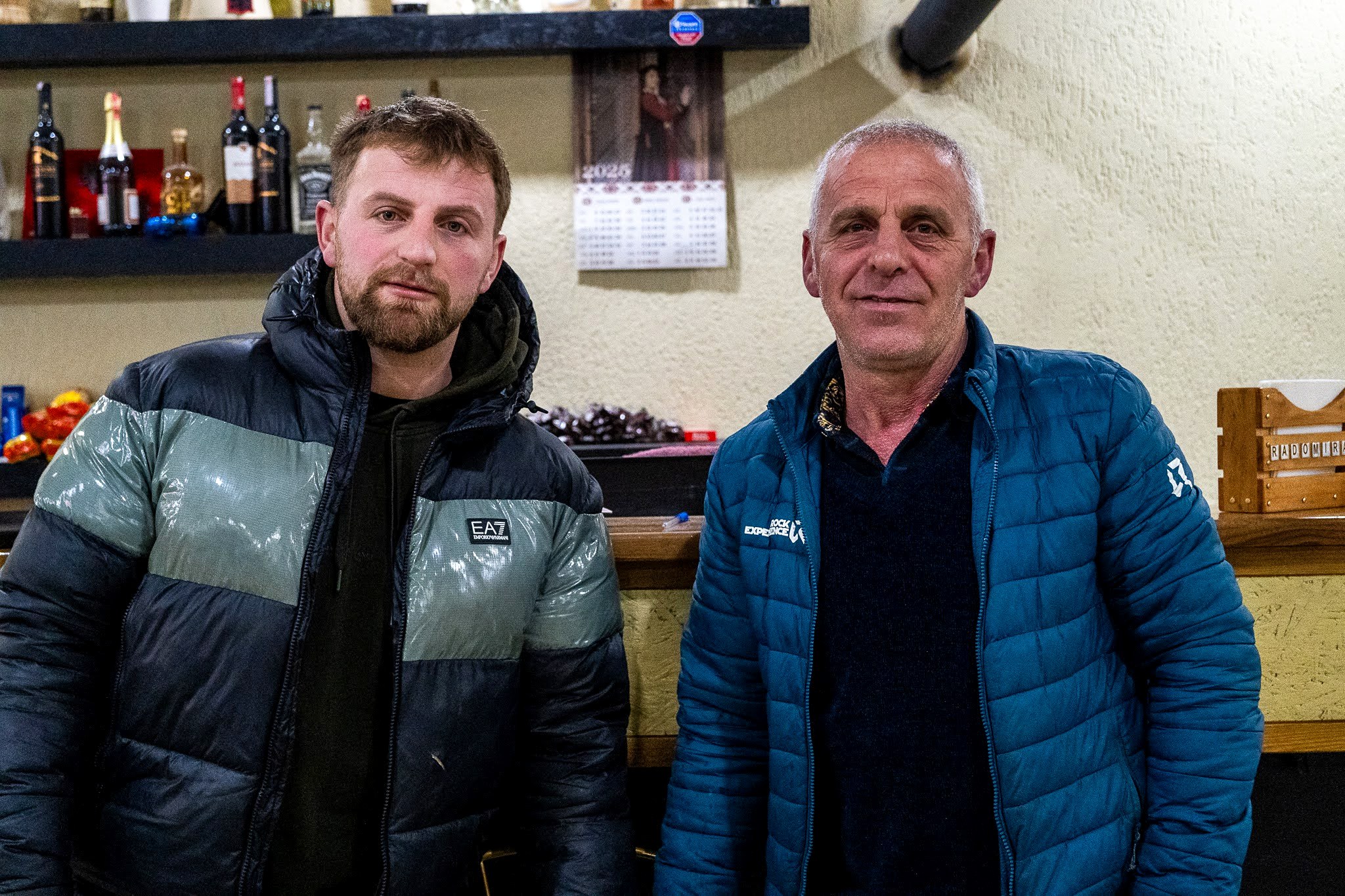 Deux hommes posant dans un petit commerce local, secteur occidental du massif du Šar, près du Korab, pendant une traversée à ski du Kosovo.