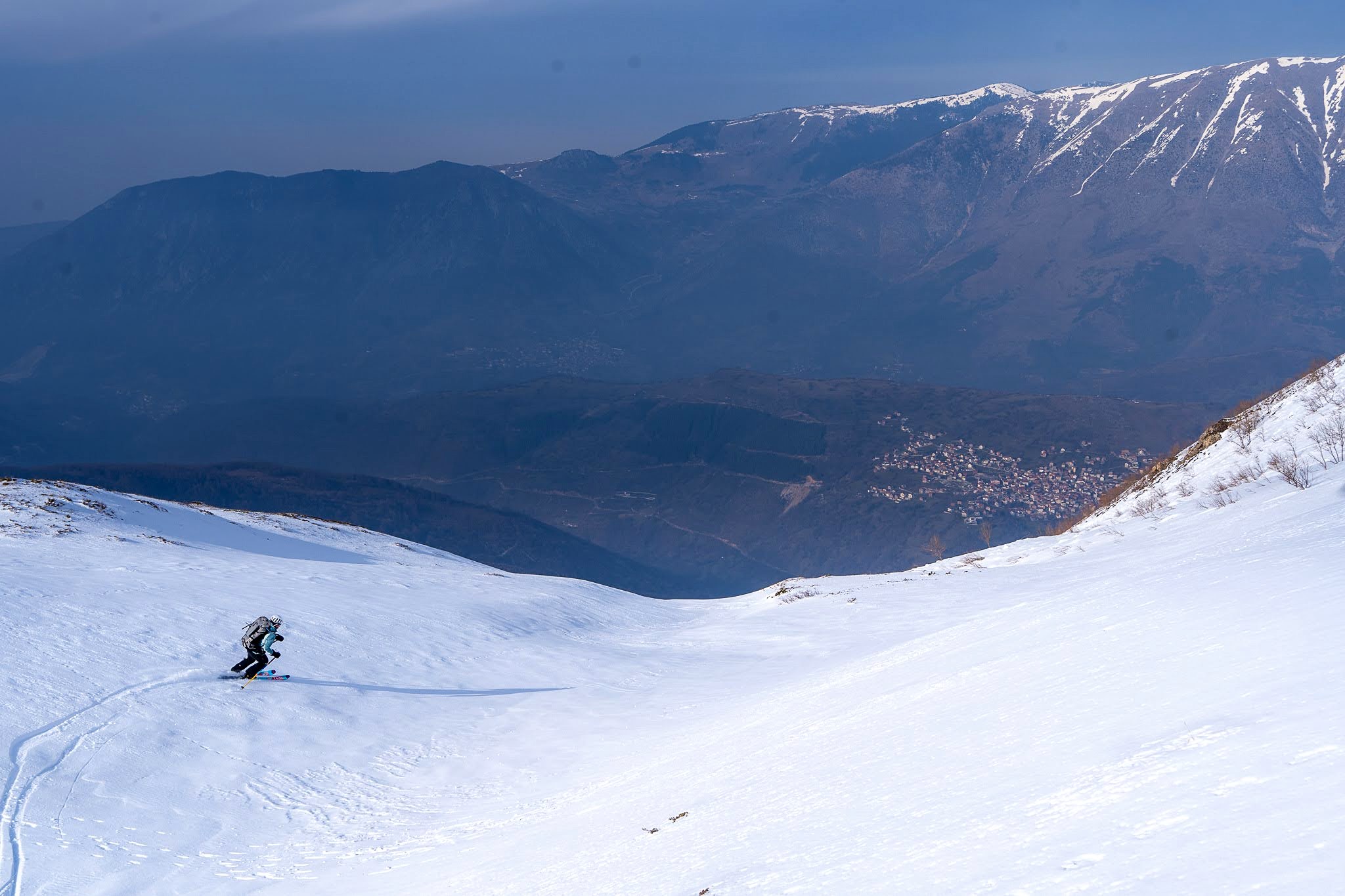 Skieur traçant une pente avec la vallée en contrebas, secteur de Dragash et Brod, massif du Šar, pendant une traversée à ski du Kosovo.