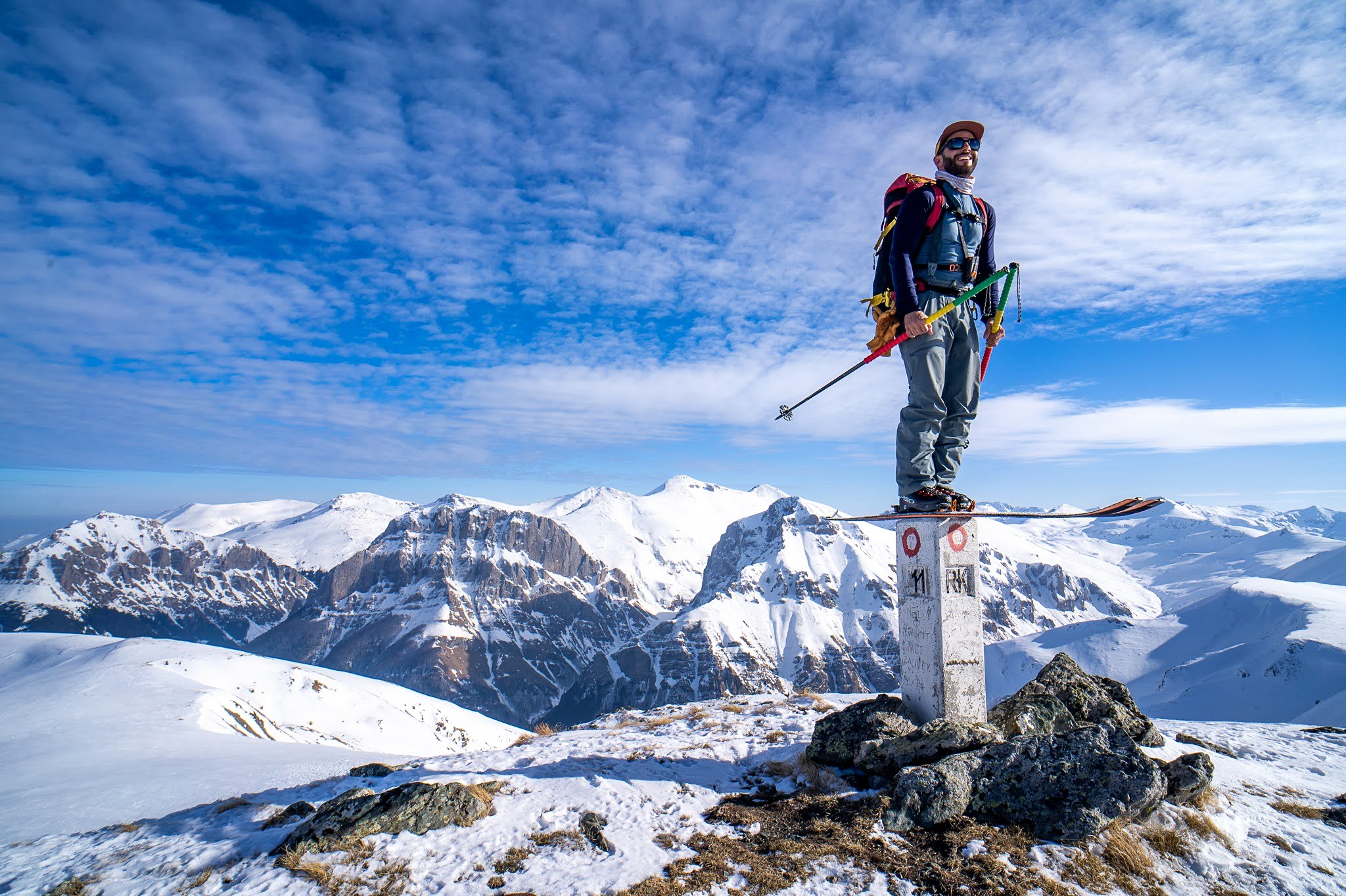 Skieur debout sur un petit sommet face aux montagnes, secteur de Dragash et Brod, massif du Šar, pendant une traversée à ski du Kosovo.