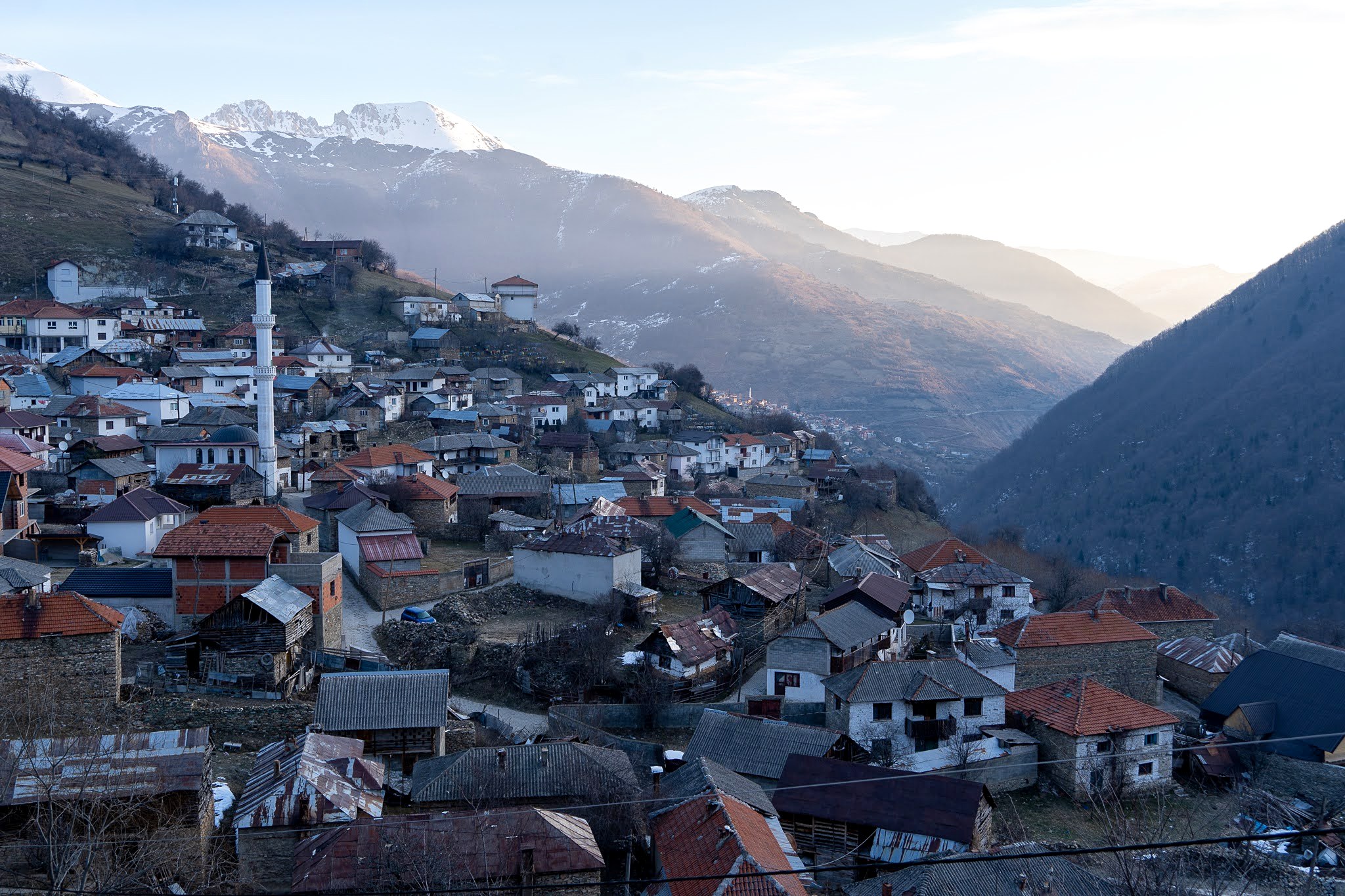Maisons serrées sur les pentes dans la lumière matinale, secteur de Dragash et Brod, massif du Šar, pendant une traversée à ski du Kosovo.